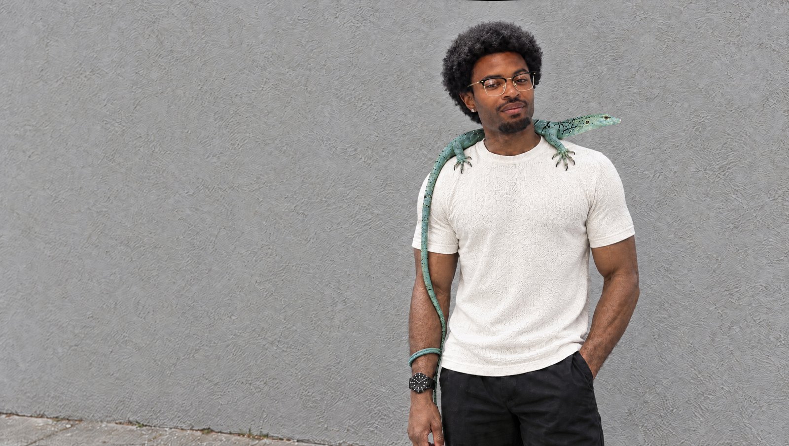 Jonah Hamilton, founder of Hatsumei, against a grey wall with Cado, his emerald tree monitor, across his shoulders