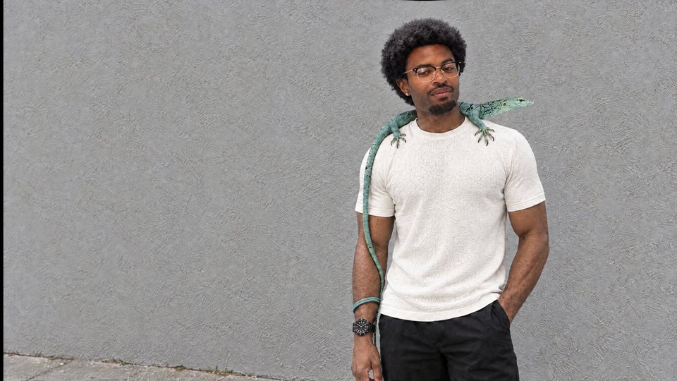 Jonah Hamilton with Cado, his emerald tree monitor, against a grey wall